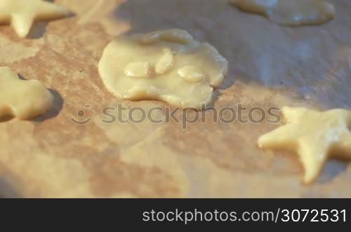 Steadicam and close-up shot of smiley cookie dough on the tray with parchment, then female hands putting star cookies there