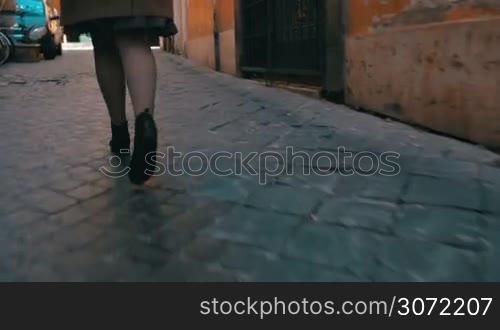 Steadicam and low angle shot of a woman running along the narrow cobblestone road. It&acute;s time to hurry up