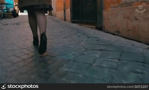 Steadicam and low angle shot of a woman running along the narrow cobblestone road. It&acute;s time to hurry up