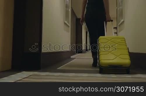 Steadicam and low angle shot of a woman traveler with suitcase in hotel corridor. She is going to check-in or leave the hotel