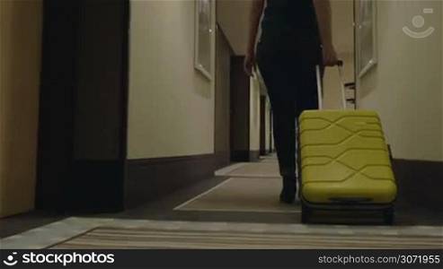 Steadicam and low angle shot of a woman traveler with suitcase in hotel corridor. She is going to check-in or leave the hotel