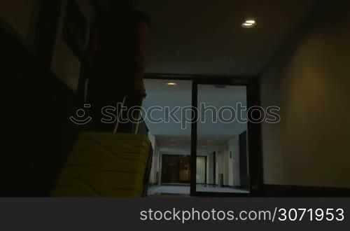 Steadicam and low angle shot of a woman walking along the hotel corridor with yelllow trolley bag