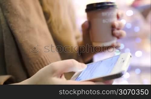 Steadicam close-up shot of a woman walking in the street with coffee and smart phone, she typing sms