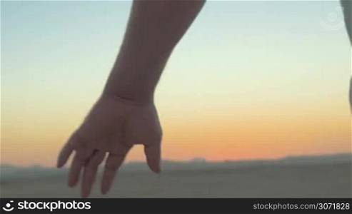 Steadicam close-up shot of romantic couple holding hands on the beach against evening sky background