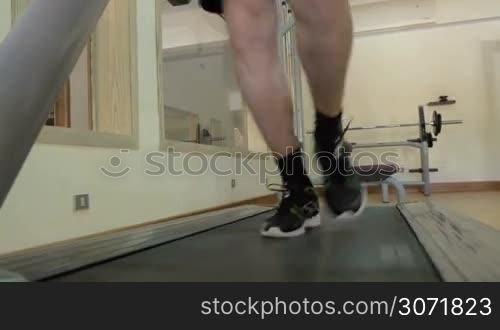 Steadicam low angle shot of male feet running on stepmill. Gym in the hotel with view to the hall