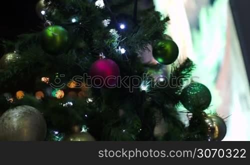 Steadicam shot of a decorated Christmas tree standing outdoor in the city at night