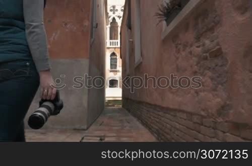 Steadicam shot of a female photographer in Venice walking between the buildings and making photos, then she coming up to the canal and continuing to shoot