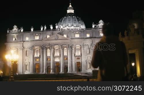 Steadicam shot of a female tourist with pad near St. Peters Basilica in Vatican City at night. She making video or photos of the greatest church of Christendom