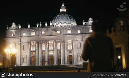 Steadicam shot of a female tourist with pad near St. Peters Basilica in Vatican City at night. She making video or photos of the greatest church of Christendom