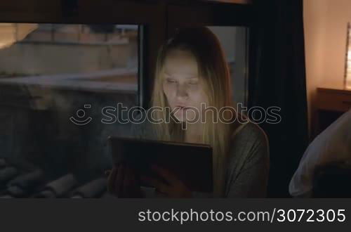 Steadicam shot of a happy and excited woman with tablet PC sitting at home in the evening and having a video chat. Connection is broken during the talk, then woman waving hand and blowing a kiss to say bye
