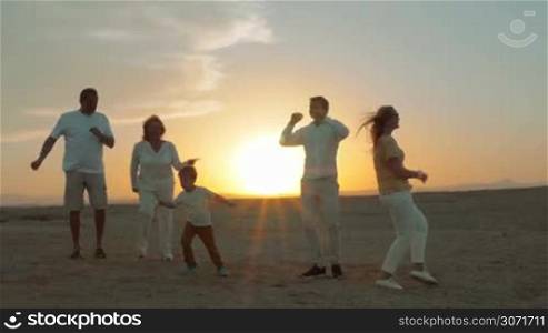 Steadicam shot of a large family dancing on the beach at sunset.