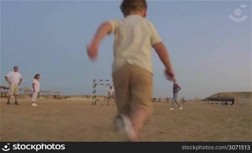 Steadicam shot of a little boy dribbling a soccer ball to the gates and preparing to kick a goal. Mother cheering him up, father is a goalkeeper