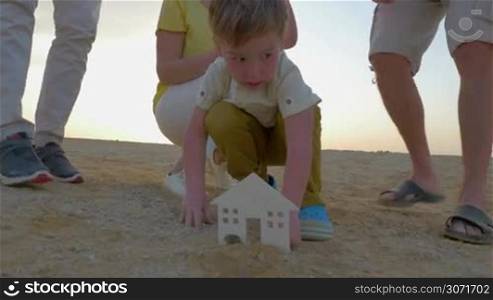 Steadicam shot of a little boy mounting a plastic figure of house in sand. His parents and grandparents are helping him.