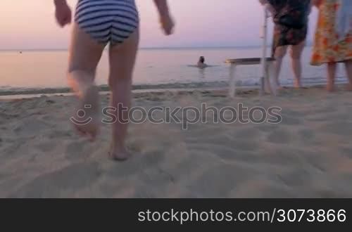 Steadicam shot of a little boy running fast on the sand walking into sea. He is eager to bathe in warm water in summer evening