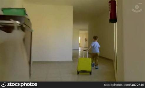 Steadicam shot of a little boy with roll-on bag running along the hotel corridor and hurrying up to reach the room