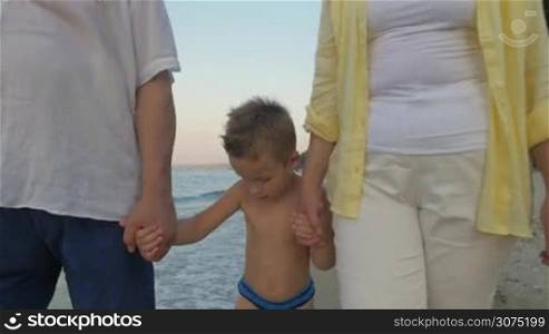 Steadicam shot of a little child with grandparents having a walk along the sea coast. Holidays at the seaside