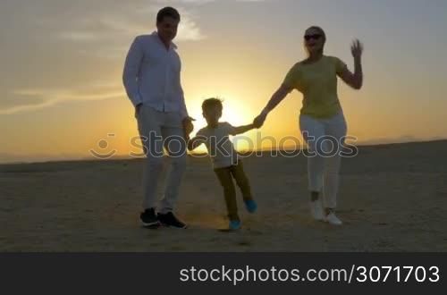 Steadicam shot of a mother, father and son holding hands and dancing on the beach at sunset.