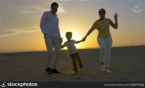 Steadicam shot of a mother, father and son holding hands and dancing on the beach at sunset.