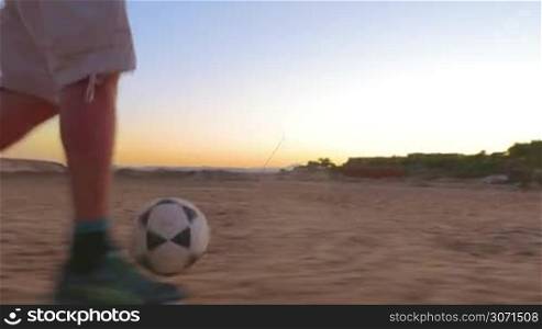 Steadicam shot of a person playing football on a sand field. He&acute;s dribbling a ball and scoring goal.