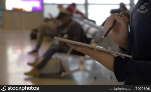 Steadicam shot of a woman busy with work on pad at the aiport lounge. She using pen to tocuh the screen. Easy business in any place with modern technologies