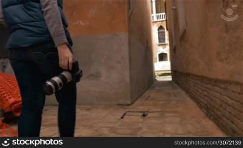 Steadicam shot of a woman photographer walking among the old houses and looking around in search of good place and angle for taking pictures
