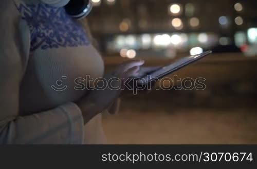 Steadicam shot of a woman typing a message on tablet computer. She walking outdoor alone in the evening