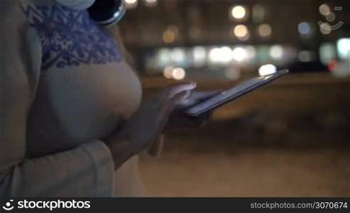 Steadicam shot of a woman typing a message on tablet computer. She walking outdoor alone in the evening