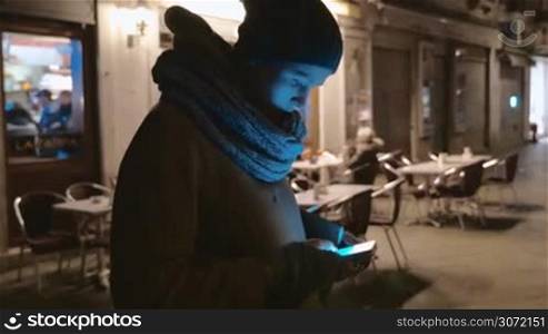 Steadicam shot of a woman using smartphone near the outdoor cafe on the small street at night