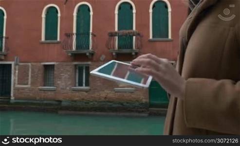 Steadicam shot of a woman with tablet computer walking in the street of Venice along the canal with old style buildings and then turning to the bridge
