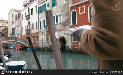 Steadicam shot of a woman with touch pad having a nice walk in Venice. She going along the canal with old worn buildings in Venice