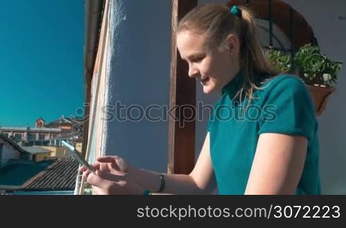 Steadicam shot of a woman working with tablet computer standing on the balcony with great city view