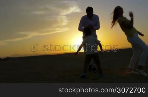 Steadicam shot of a young couple and their son dancing on the beach. The setting sun is on the background.