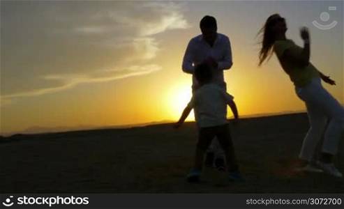 Steadicam shot of a young couple and their son dancing on the beach. The setting sun is on the background.