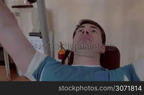 Steadicam shot of a young man in the gym doing chest press with great efforts. Then he taking off one weight disk