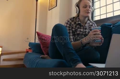Steadicam shot of a young woman using heaphones and laptop for video chat. She having a drink and emotional talk