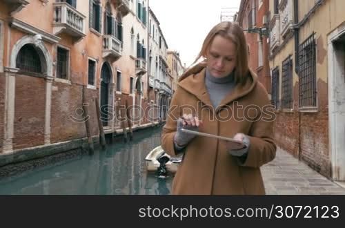 Steadicam shot of a young woman using tablet PC while walking in Venice. Then following view of canal and back view a girl