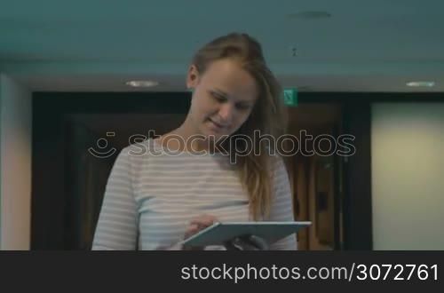 Steadicam shot of a young woman walking in some building with tablet in hands. She&acute;s smiling while chatting with friends.
