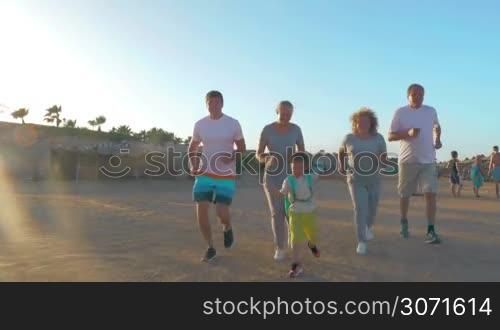 Steadicam shot of big family jogging on the beach. Son, parents and grandparents keeping fit on vacation