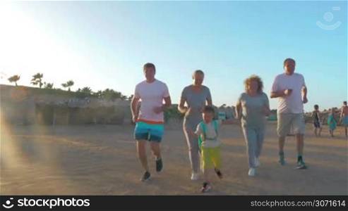 Steadicam shot of big family jogging on the beach. Son, parents and grandparents keeping fit on vacation