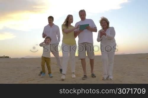 Steadicam shot of big family on vacation with modern gadgets. Everyone is busy with his device. Boy talking on cell phone, father and grandmother using smart phones while mother and grandpa walking with pad. Technology dependence