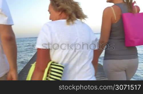 Steadicam shot of big family with colorful shopping bags walking along the wooden pier in the sea