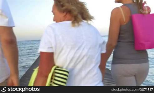 Steadicam shot of big family with colorful shopping bags walking along the wooden pier in the sea