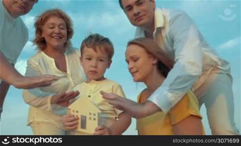 Steadicam shot of big family with small wooden house. Boy holding it and they all protecting it with hands. Family hearth or insurance concept