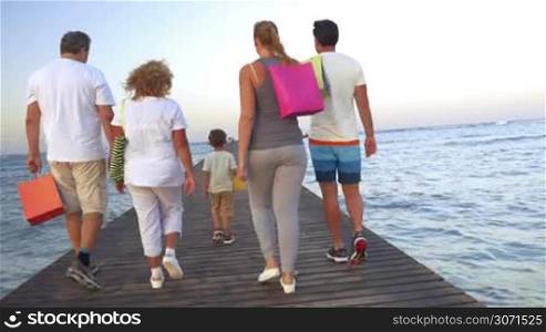 Steadicam shot of big happy family with child walking on the pier after shopping. They turning to the camera, smiling and waving hands