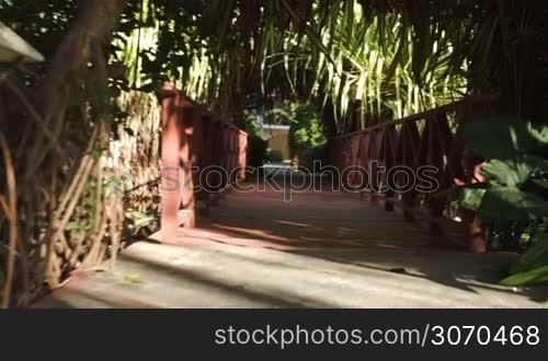 Steadicam shot of crossing a wooden bridge under palm shed and path leading to the house