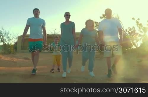 Steadicam shot of evening hiking on vacation. Parents, little son and grandparents holding hands while walking outdoor