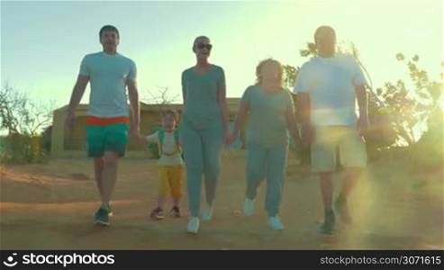 Steadicam shot of evening hiking on vacation. Parents, little son and grandparents holding hands while walking outdoor