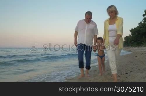 Steadicam shot of grandparents and grandson holding hands and walking barefoot along the shore