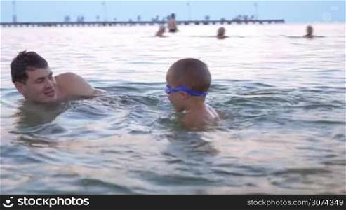 Steadicam shot of little boy in goggles swimming in the sea with his parents.