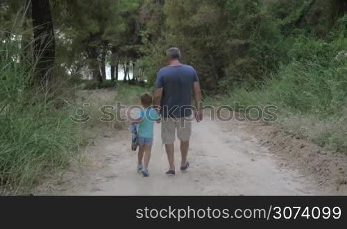 Steadicam shot of little boy walking by hand with grandfather in the wood. Outing in the forest with grandpa